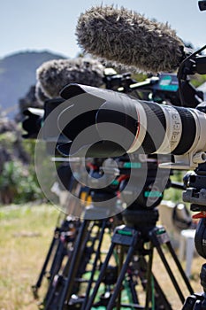 Row of professional video cameras outdoor. Camera with microphone on tripod. TV reality show filming. News and reportage concept.