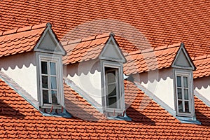 Row of renovated old style roof windows covered with new red roof tiles and snow guards on top of suburban family house