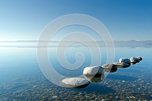 A row of rocks carefully balanced on the surface of a body of water, A view of a calm lake with smooth stones, reflecting a clear