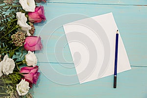 Row of roses on wooden background with space for message. Mother`s Day background. empty paper sheet on turquoise rustic table fro