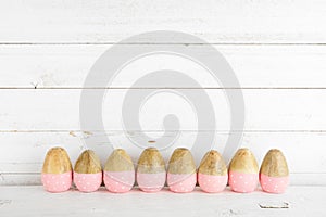 Row of rustic pink painted wood Easter Eggs against a white wood background