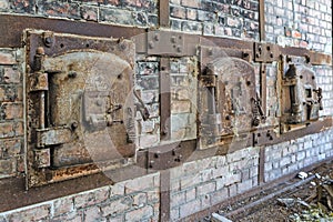 A row of rusty old metal hatch doors of a red brick kiln.