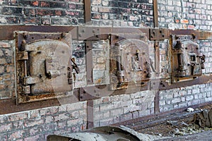 A row of rusty old metal hatch doors of a red brick kiln.