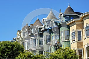 Row of seperate colorful house buildings or homes with green and gray facades and front yard trees with spure or turret