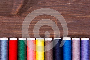 Row of sewing thread in different colors on wood