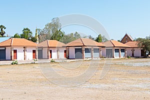 Row of small houses or booth in bright sunlight beside dry grass.
