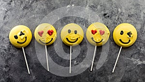 A row of smiley face emoji merengues on lollipop sticks.