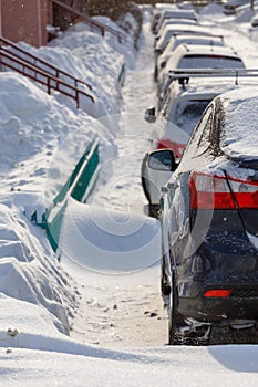 row of snow drifted cars in a row along the street near residential building at winter day snowfall