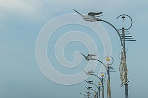 Row of the street lamps in bird shaped with the white clouds background. Perspective street lamps aligned with beautiful blue sky