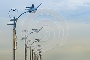 Row of the street lamps in bird shaped with the white clouds background. Perspective street lamps aligned with beautiful blue sky