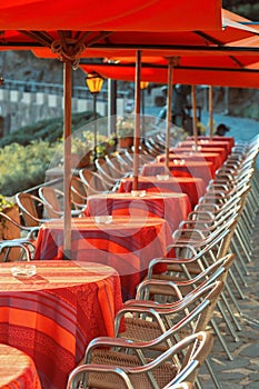 A row of tables with red tablecloths on the open terrace of a restaurant in the seaside town.