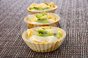 Row of tartlets with kiwi, banana and yogurt on mat