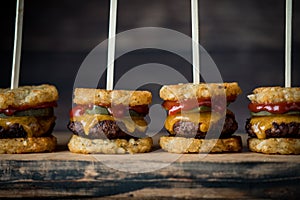 A row of tater beef slider skewers on a wooden board, against a dark background.