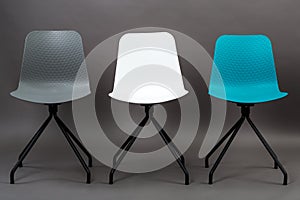 Row of three color plastic chairs isolated on gray background. Furniture series.