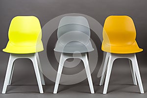 Row of three color plastic chairs isolated on gray background. Furniture series.