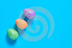 Row of three colorful eggs with glitters lies on blue desk on kitchen. Easter concept