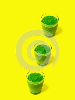 Row of three glasses of leafy greens smoothies spinach vegetables fruits on bright sunny yellow background. Healthy diet detox