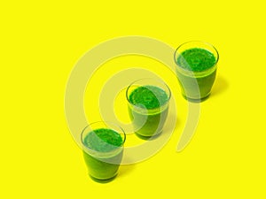 Row of three glasses of leafy greens smoothies spinach vegetables fruits on bright sunny yellow background. Healthy diet detox