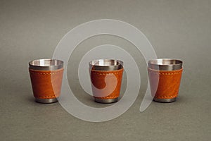 Row of three metallic shot glasses. travel shot glass for alcohol with leather casing over the stainless steel. personal accessory