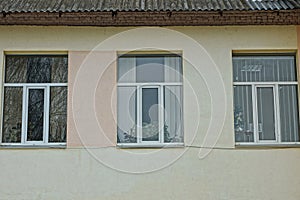 A row of three white windows on a brown concrete wall