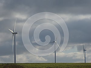 Row of three wind turbines in a green field with a cloudy sky in the background