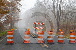 Row of tightly spaced orange traffic barrels barricading a road disappearing into a foggy autumn landscape