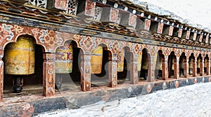 Row of traditional yellow Buddhist prayer wheels in the wall, Bhutan