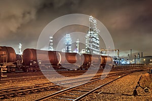 Row of train wagons with an illuminated oil refinery at night in Port of Antwerp, Belgium