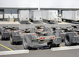 Row of trolleys with axles and fifth wheel tow hitch for semi trucks trains standing on the warehouse parking lot with semi