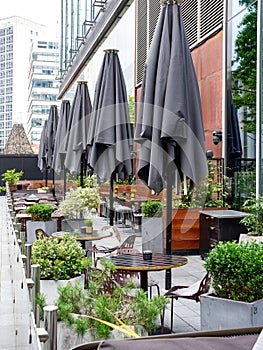 a row of umbrella's folded at an outdoor restaurant in the city with tables and chairs