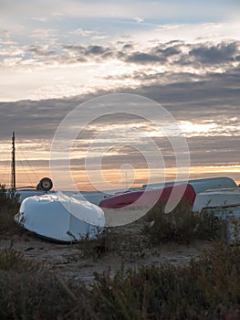 Row of upturned beach boats flat on land with dramatic sun set s