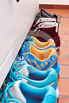 Row of used shoes lined up partially under shoe cabinet inside apartment side view