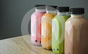 A row of various bobble tea in a plastic bottles on wooden table with black color background, copy space