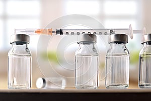Row of vials and syringe on table with background windows