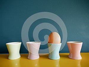 Row of vintage pastel egg cups on yellow sideboard against blue background.