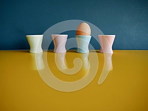 Row of vintage pastel egg cups on yellow sideboard against blue background.