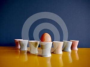 Row of vintage pastel egg cups on yellow sideboard against blue background.