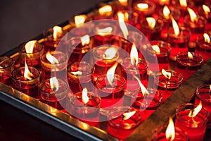 Row of votive religious red candle with flame in glass