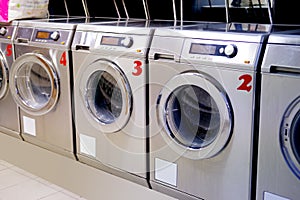 Row of washing machines in public city self-service laundromat, clean linen concept, washing clothes, bachelor life