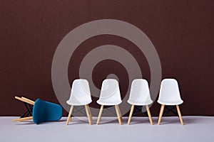Row of white chairs and a blue one falling down. Business concept