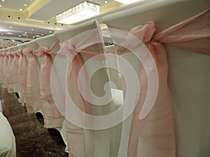 Row of white chairs decorated with pink bows