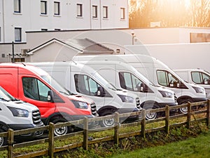 Row of white commercial vans in a dealership for sale or rent and one red color. Used and new busses. Transport industry