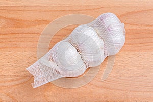 Row white garlic bulbs in net package place on wooden table, gen