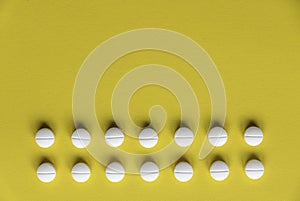 A row of white medical pills on yellow background with copy space