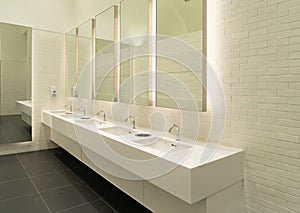 Row of white modern marble ceramic wash basin in public toilet, restroom in restaurant or hotel or shopping mall, interior