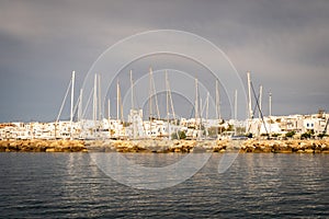 Row of white sailboats docked in Naoussa coastal village port Paros Island during golden hour with typical whitewashed houses.