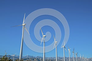 Row of windmills with three blades against blue sky on a sunny day.