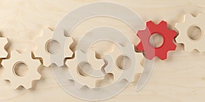 Row of wooden cogwheels or gears with one red on wooden table top view from above, business process, team or teamwork concept