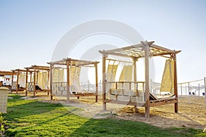 Row of wooden furniture for rest with curtains, deck chair bed, gazebo on sand beach with grass lawn, tropical sea luxury resort.