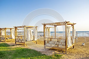 Row of wooden furniture for rest with curtains, deck chair bed, gazebo on sand beach with grass lawn, tropical sea luxury resort.